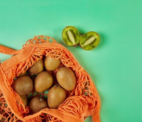 Flat lay Mesh grocery shopping eco friendly bag with kiwi on green canvas background